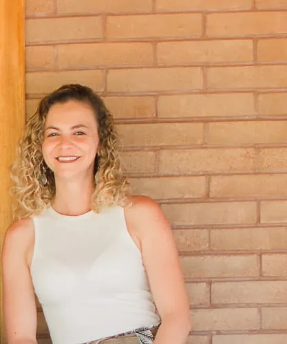Káccia, proprietária e gestora do Natureza Interior, sorrindo diante de uma parede de tijolinho