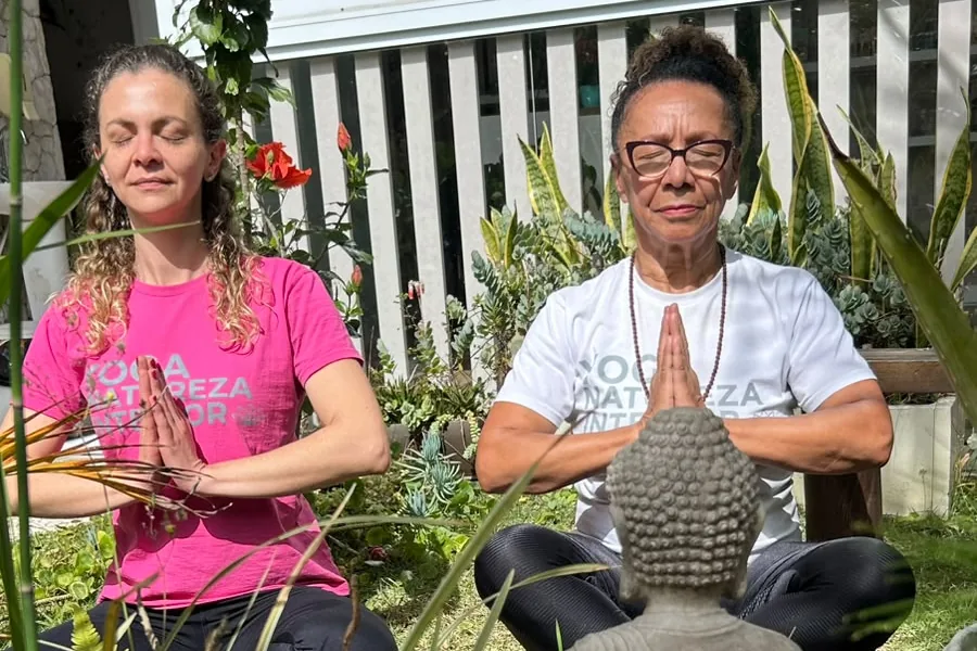 Káccia e Rô meditando lado a lado, com uma estátua de Buda em primeiro plano