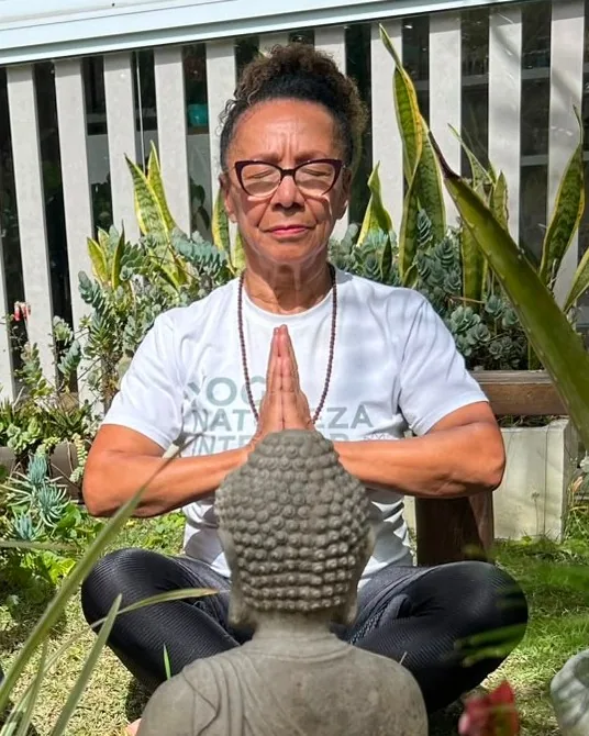 Rô Martins, professora de Yoga, meditando diante de uma estátua de Buda no jardim do Natureza Interior